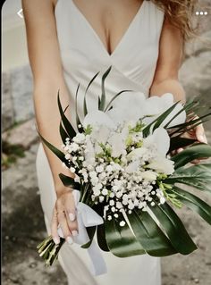 a woman in a white dress holding a bouquet of flowers and greenery on her wedding day