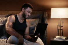 a man sitting on a bed using a laptop computer in his hand and smiling at the camera