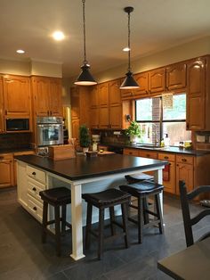 a large kitchen with wooden cabinets and black counter tops, two stools at the island