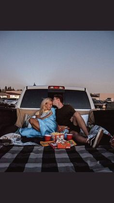 a man and woman sitting in the back of a pickup truck with food on the bed