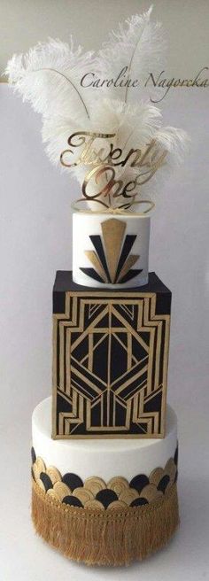 a three tiered cake decorated with black and gold decorations, feathers and calligraphy