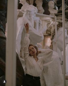 a woman is standing in front of some white sculptures and posing for the camera with her hands up