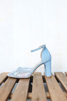 a pair of blue high heeled shoes sitting on top of a wooden bench next to a white wall