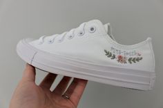 someone is holding their white converse sneakers with embroidered flowers on the bottom and lace at the toe