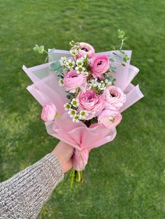 a person holding a bouquet of pink roses and daisies in their hand on the grass