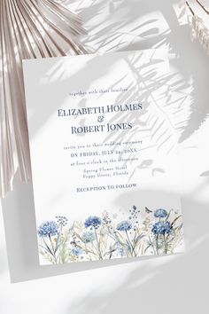 a wedding card with blue flowers and leaves on the front, next to a palm tree