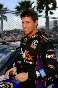 a man standing next to a car in front of a fence