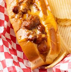 a chili dog with cheese and ketchup in a basket next to some potato chips