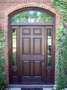 the front door is made of wood and has an arched glass window above it, along with potted plants on either side