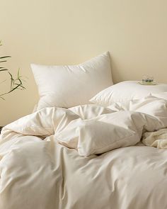 an unmade bed with white sheets and pillows on the floor next to a potted plant