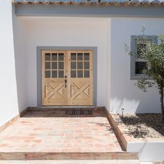 two wooden doors on the side of a white building with red brick steps leading up to it