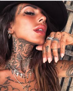 a woman with tattoos on her neck and chest wearing a black hat, necklaces and rings