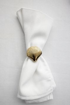 a white napkin with a gold shell on it's side, resting on top of a folded napkin