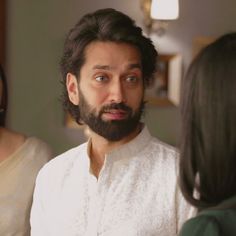 a man with a beard standing in front of two women looking at something on the table