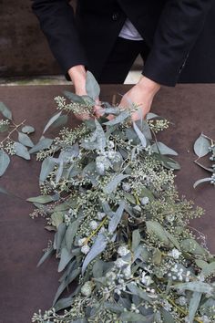 a man in a suit is arranging flowers and leaves on the ground with his hands