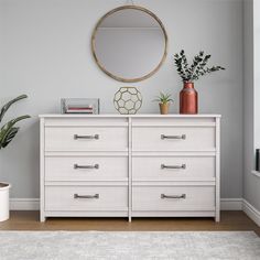 a white dresser with two potted plants and a round mirror on the wall above it