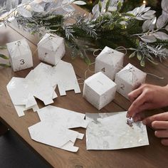 someone is cutting out some white paper for christmas decorations on a table with greenery