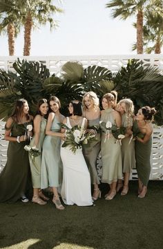 a group of women standing next to each other in front of palm trees and bushes