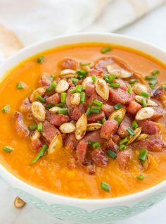 a white bowl filled with carrot soup topped with bacon and green onion garnish