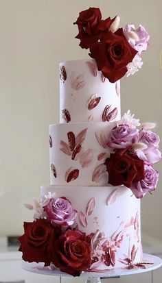 a three tiered wedding cake with red and pink flowers