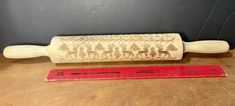 a rolling pin with reindeer and trees on it sitting next to a ruler that says christmas