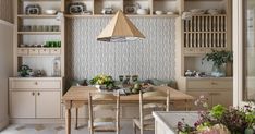 a dining room table and chairs in front of a shelf with dishes on it,