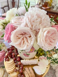 a table topped with flowers and crackers next to a vase filled with pink roses