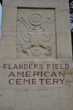 the sign on the building says flanders's field american cemetery, located in front of an eagle