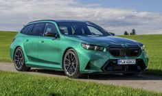 a green bmw suv parked on the side of a road in front of a grassy field