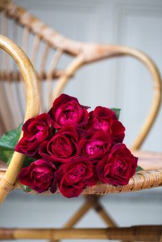 a bouquet of red roses sitting on top of a wooden chair next to a wicker chair