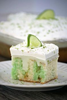 a piece of cake on a white plate with a lime slice and whipped cream frosting