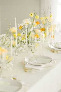 the table is set with yellow and white flowers in vases, candles, and plates