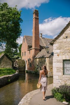 a woman walking down a sidewalk next to a river with a brick building in the background