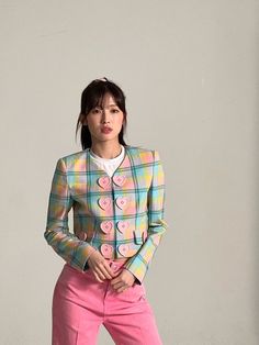 a woman in pink pants and a plaid jacket with hearts on the front, standing against a gray wall