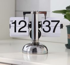 an alarm clock sitting on top of a white counter next to a potted plant