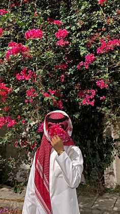 a man standing in front of a bush with pink flowers on it's head