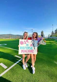 two girls holding up signs on a soccer field with the words defense machine written on them