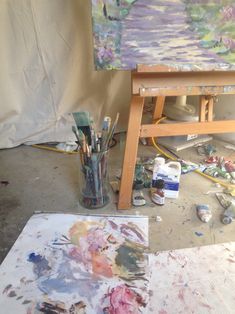 an artist's easel with paint and brushes on the floor next to it