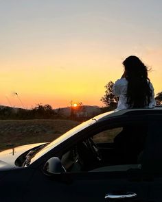 a woman sitting on top of a car in the sunset