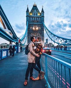 a man and woman are kissing in front of the tower bridge at dusk, london