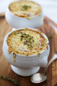 two white bowls filled with food sitting on top of a wooden cutting board next to a spoon