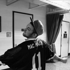 a man with a baseball cap on his head sitting in a locker room wearing a jersey that says mac miller