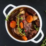 a white bowl filled with stew and carrots on top of a black countertop