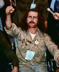 a man with long hair and beard sitting in a wheel chair holding up his fist