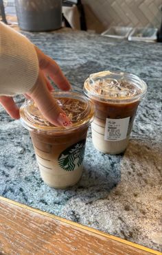 two cups of coffee on a table with one being put in the cup by someone's hand