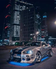 a silver sports car parked in the middle of a city at night with lights on