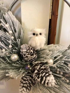 an owl sitting on top of a wreath with pine cones and balls in it's paws