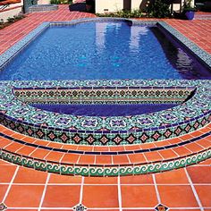 an outdoor swimming pool surrounded by red tile and blue tiles with designs on the sides