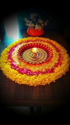 a flower arrangement on a table with a lit candle in the center and flowers around it