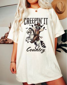 Enjoy the spirit of fall with our Raccoon Cowboy Halloween Shirt for Women, featuring a charming western aesthetic. This cute cowgirl shirt is perfect for celebrating Halloween with a unique twist. Made from soft, high-quality Comfort Colors® fabric, this country graphic tee ensures a comfortable fit, making it ideal for all-day wear. Whether you're heading to a fall festival, a Halloween party, or just enjoying a casual day out, this adorable raccoon cowboy shirt adds a touch of fun and style t Western Style Graphic Print Shirt For Fall, Western Style Graphic Print Fall Shirt, Unique Fall Fashion, Country Graphic Tees, Cowboy Halloween, Halloween Cowboy, Fall Fashion Colors, Cute Cowgirl, Cowboy Design